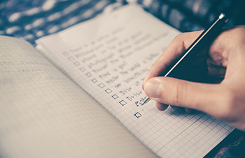 a hand holds a pen and checks off items on a list in a notebook